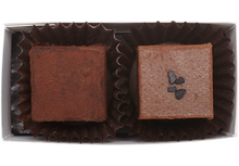 Load image into Gallery viewer, Above view and inside the rectangle box, 1 cube shaped dark salted caramel truffle (coated in cocoa powder) and 1 cube shaped milk caramel truffle with a few flakes of black salt in the center. Each truffle is in a brown paper candy cup.