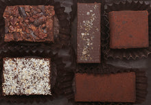 Load image into Gallery viewer, View from above of the opened “Quintet Box” with 5 chocolate truffles arranged in paper candy cups: Almond butter, Cacao Nib, Lime, Coconut and Mocha Cinnamon