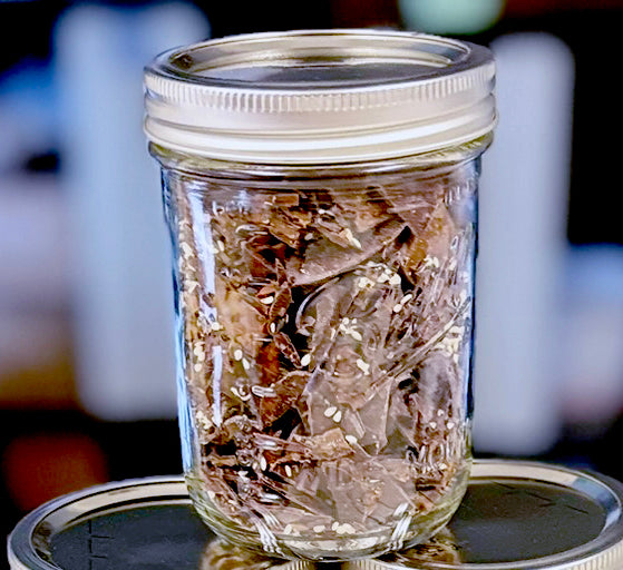 Black Sesame Seed Toffee Brittle Bits inside of glass Bell jar with sliver lid.