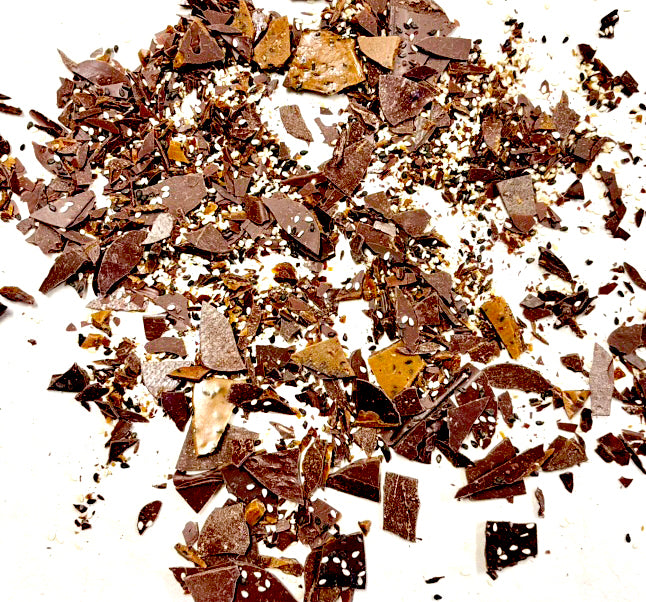 Black Sesame Seed Toffee Brittle Bits spread out on a piece of white paper