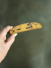 Load image into Gallery viewer, Hand holding a long cookie with bits of chocolate against a blurred background