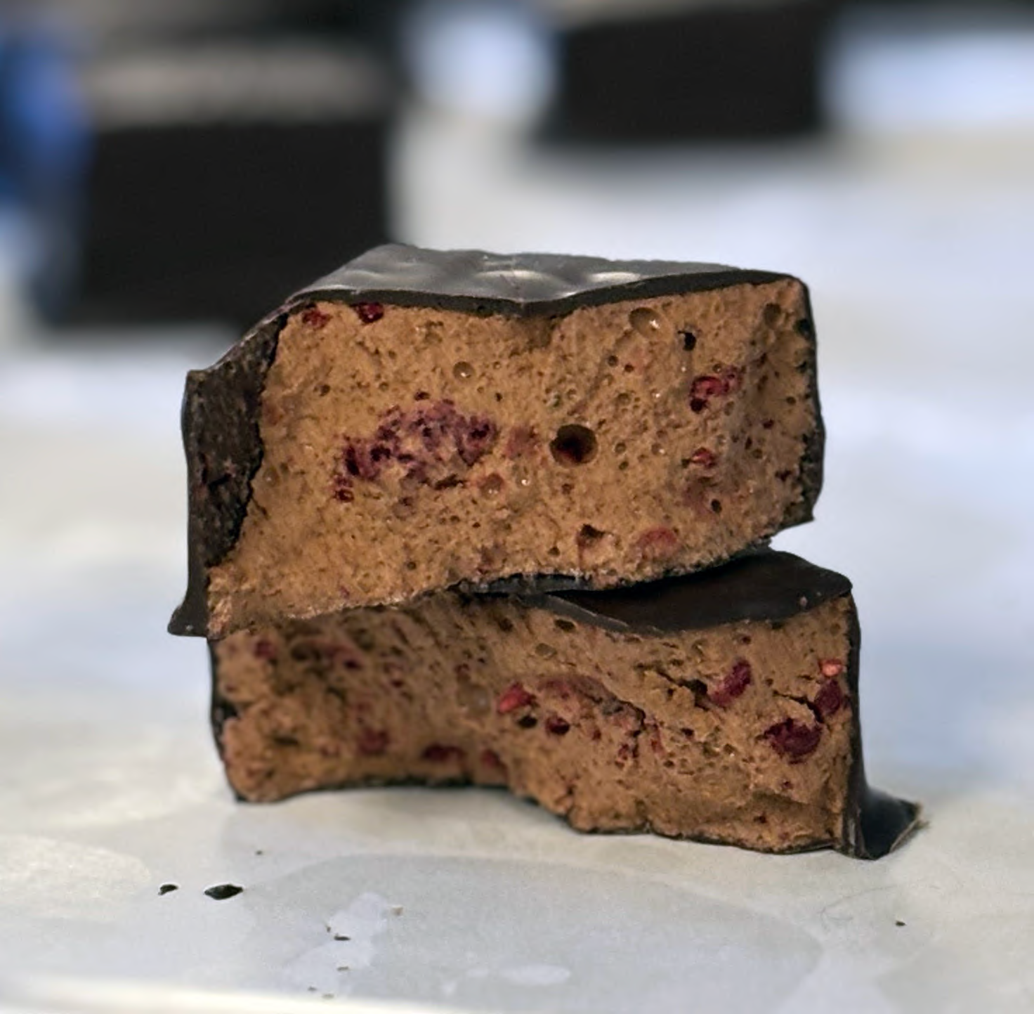 Two chocolate-covered raspberry rose double chocolate marshmallows stacked on a white surface with a blurred background
