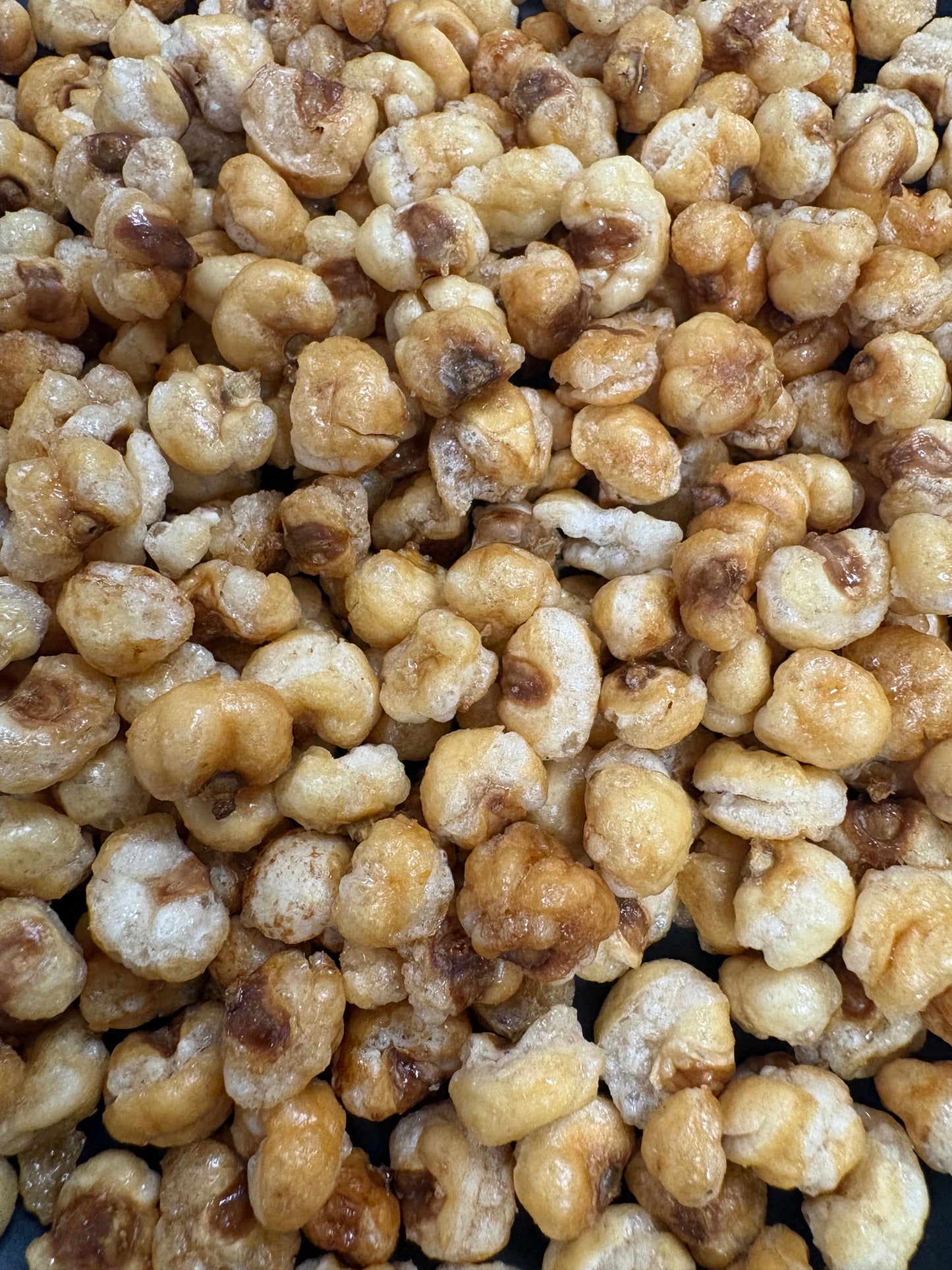 A close-up view of caramelized popcorn kernels piled together, showing golden-brown and cream tones with some darker toasted areas.