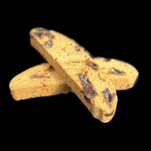 Load image into Gallery viewer, Two chocolate 2 pieces of toffee nib brittle biscotti criss-cross each other. The toffee bits can be seen inside the biscotti on a black background