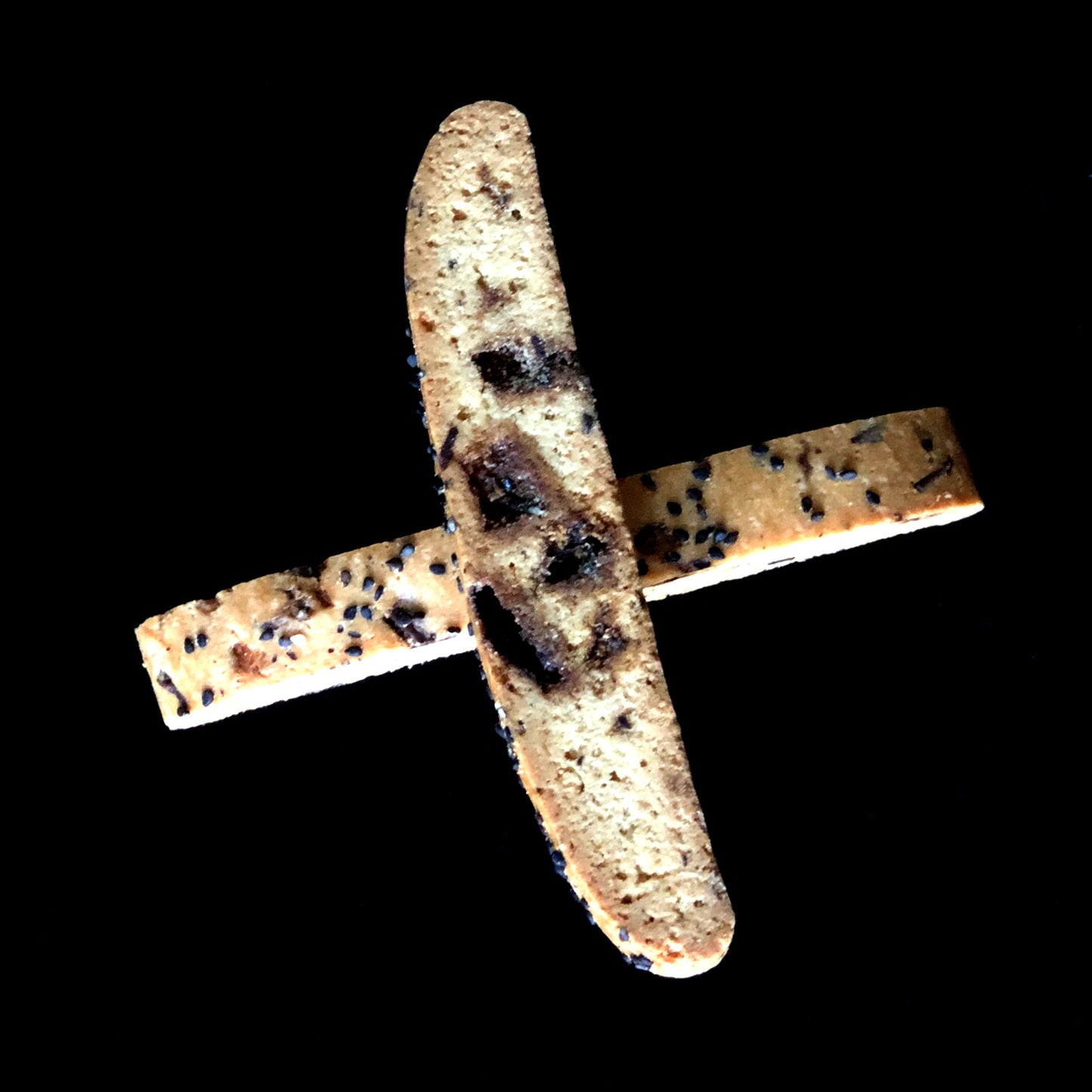 2 pieces of sesame brittle biscotti criss-cross each other. The toffee bits can be seen inside the biscotti.