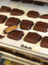 Load image into Gallery viewer, Production sheet pan with pieces of chocolate covered honeycomb candy out of the enrober. Once piece broken open to expose honeycomb candy inside. 