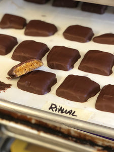Production sheet pan with pieces of chocolate covered honeycomb candy out of the enrober. Once piece broken open to expose honeycomb candy inside. 
