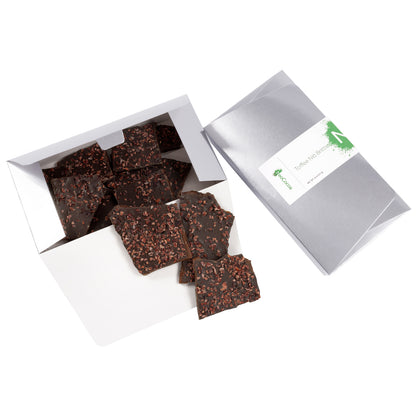 2 dimensional angle of opened 8oz silver box with title of “Toffee Nib Brittle” with green NeoCocoa logo and 8oz pile candy pieces inside the box bottom and 3 pieces of candy spilling out.