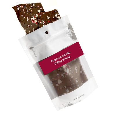 Peppermint nib brittle pouring out of 3oz sized bag with orange label stating “Peppermint Nib Toffee Brittle” and NeoCocoa logo.